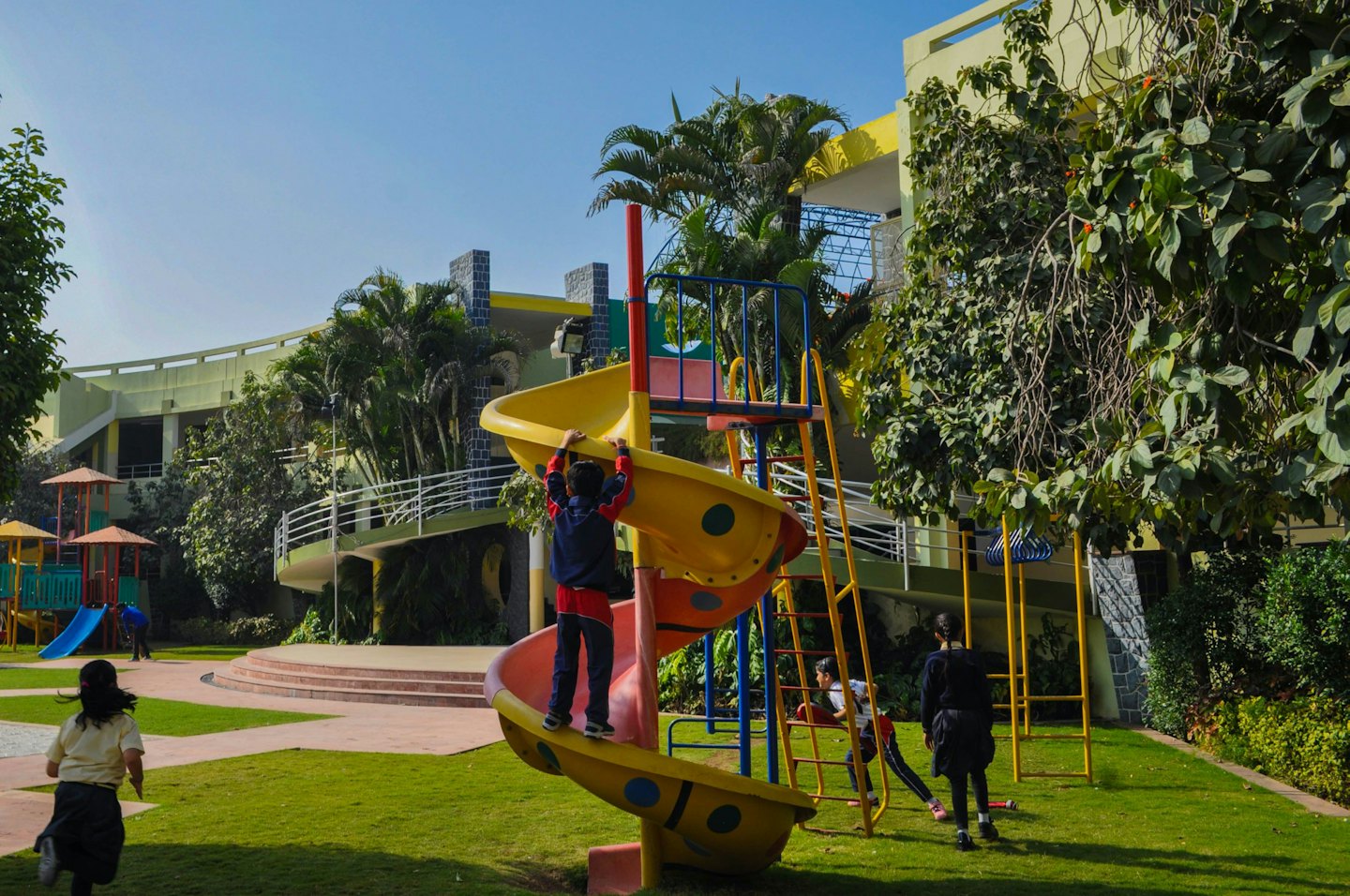 Niños jugando en un parque infantil soleado con tobogán y estructuras para trepar.