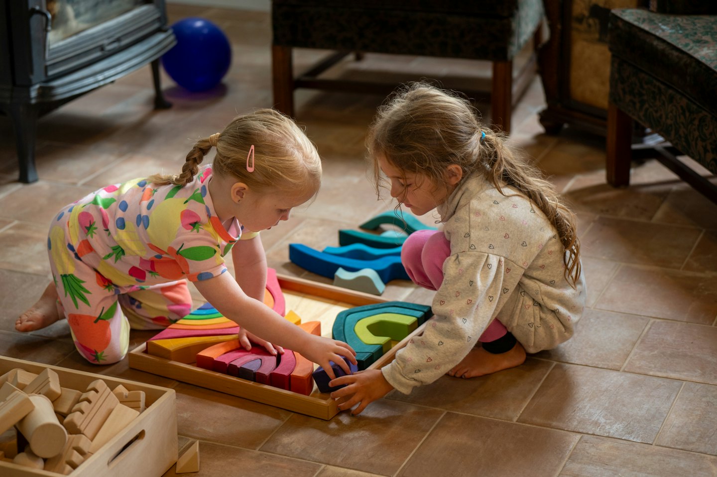 Dos niñas jugando con bloques de madera de colores en el suelo.